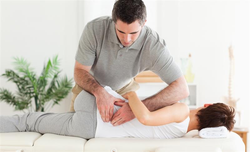 A therapist performs a chiropractic adjustment on a patient lying on a treatment table in a bright, modern clinic.